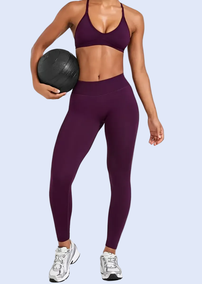 Person wearing purple athletic leggings and sports bra holding a black medicine ball on a white background
