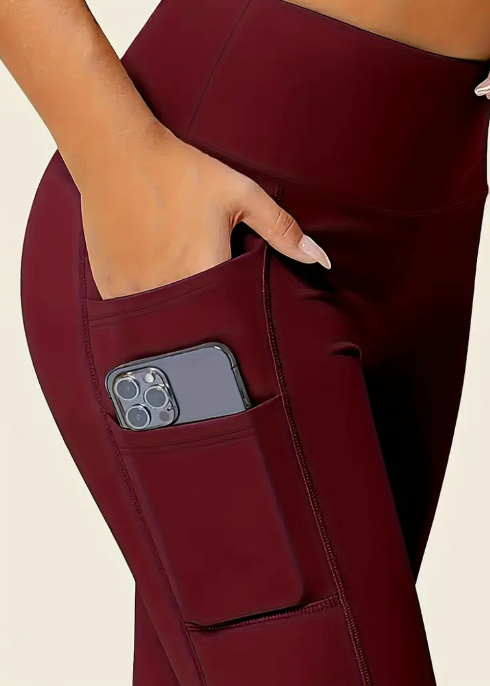 Maroon pants with a pocket holding a phone on a beige background