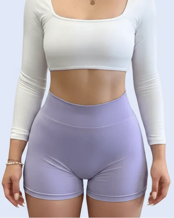 Person wearing a white long-sleeve crop top and purple leggings taking a mirror selfie.