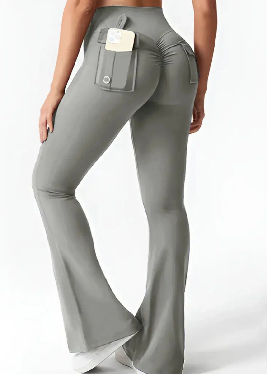 Back view of woman wearing gray flared activewear pants with pockets, holding smartphone