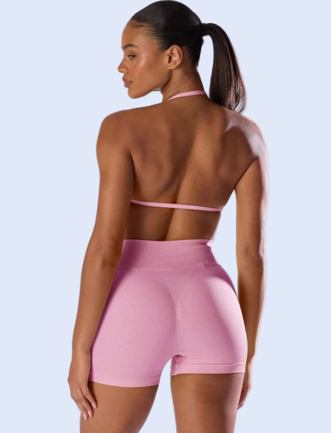 Woman wearing a pink sports bra and shorts set on a plain background