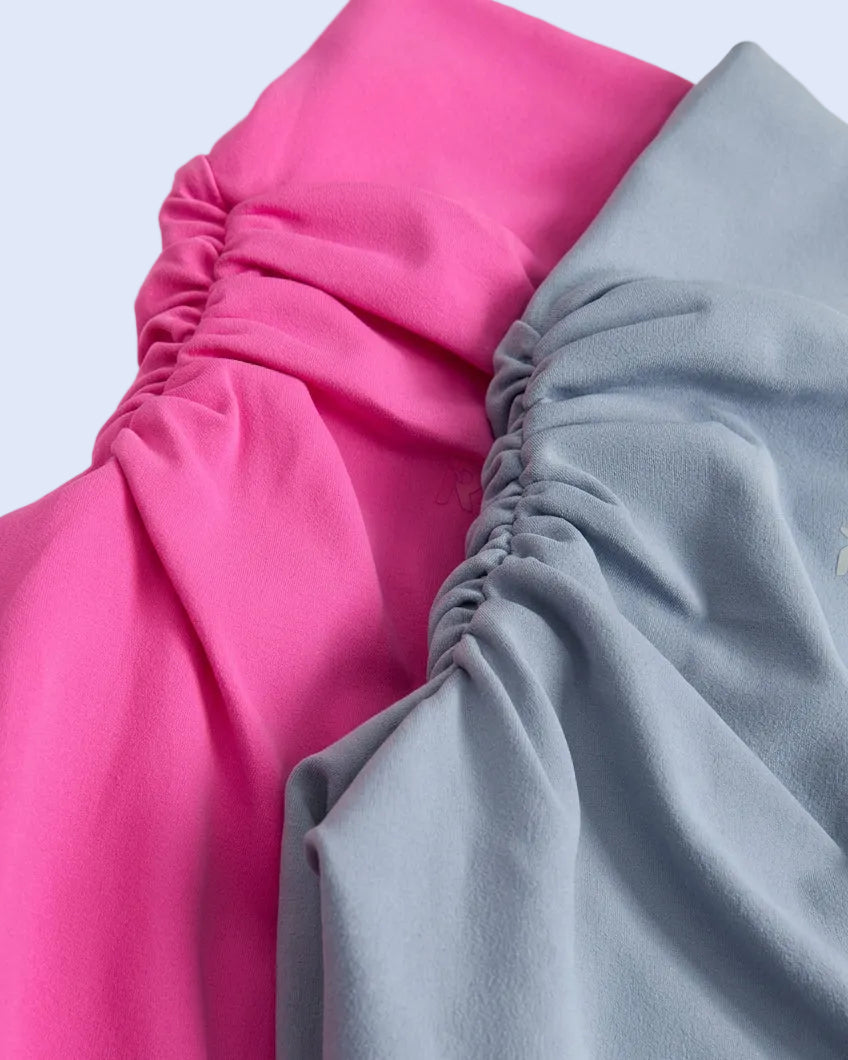 Three pairs of ruched shorts in olive green, bright pink, and light blue, folded and stacked on a clear plastic surface.