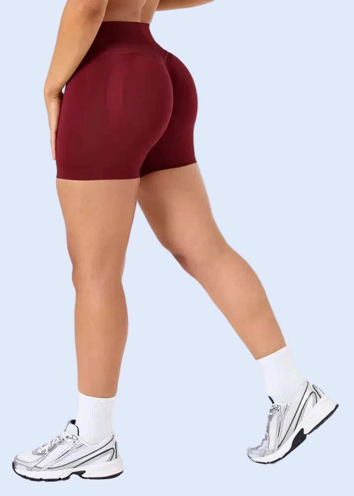 Person wearing maroon high-waisted shorts and white sneakers on a light gray background