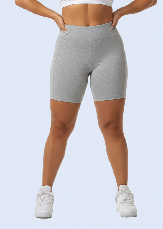 Woman wearing a white sports bra and gray shorts on a light blue background