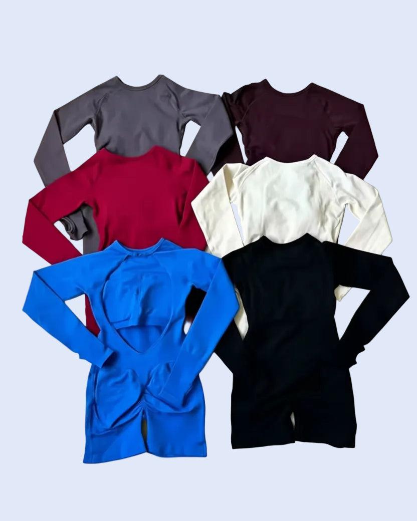 Six long-sleeve knit tops in different colors are laid flat on a light fabric surface. The colors visible are gray, burgundy, red, off-white, bright blue, and black.
