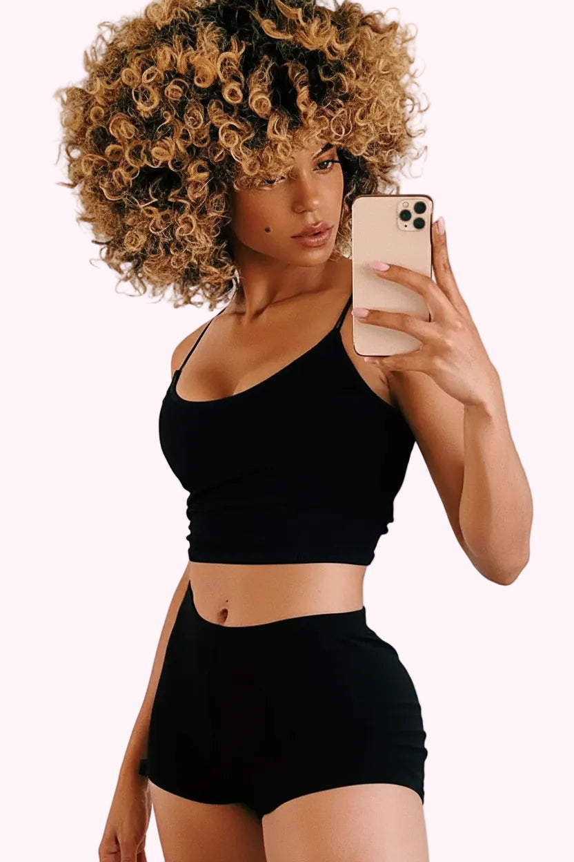 Woman taking a selfie wearing a black sports bra and shorts on a beige background