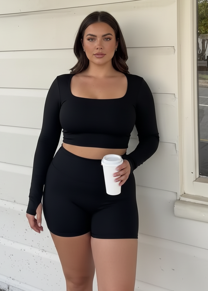 Woman in black athletic wear standing against a white wall.
