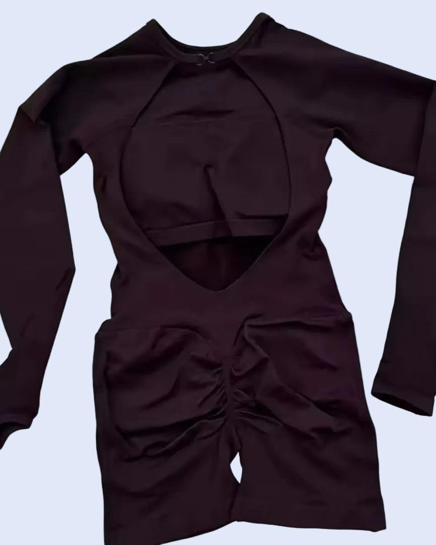 A dark plum long-sleeve athletic romper with a large chest cutout, a horizontal waist cutout, and gathered ruching at the front, laid flat on a light gray background.