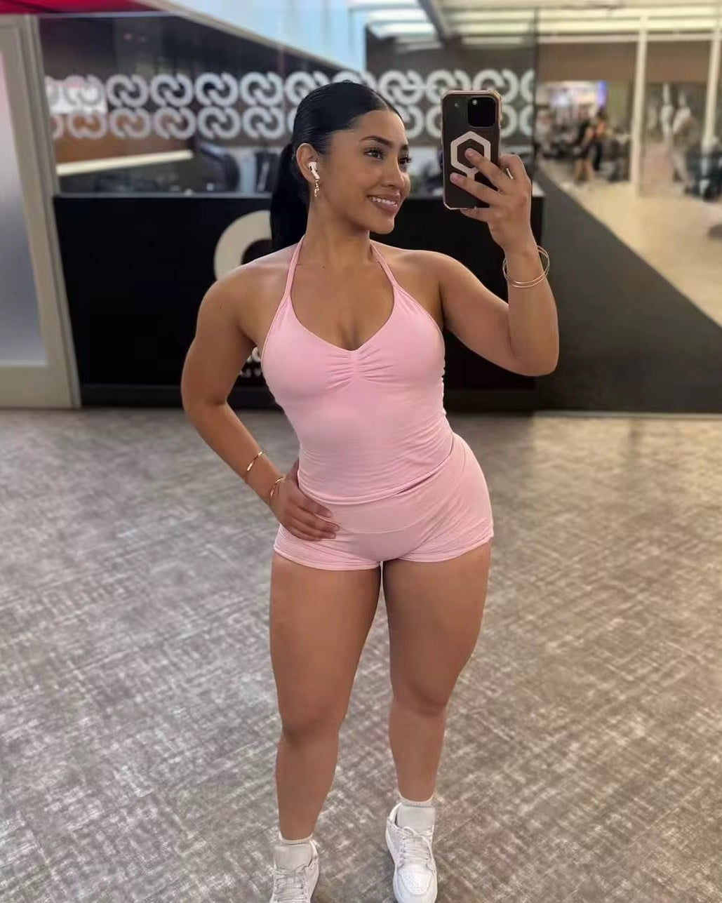 Woman taking a mirror selfie in a pink athletic outfit in an indoor setting.