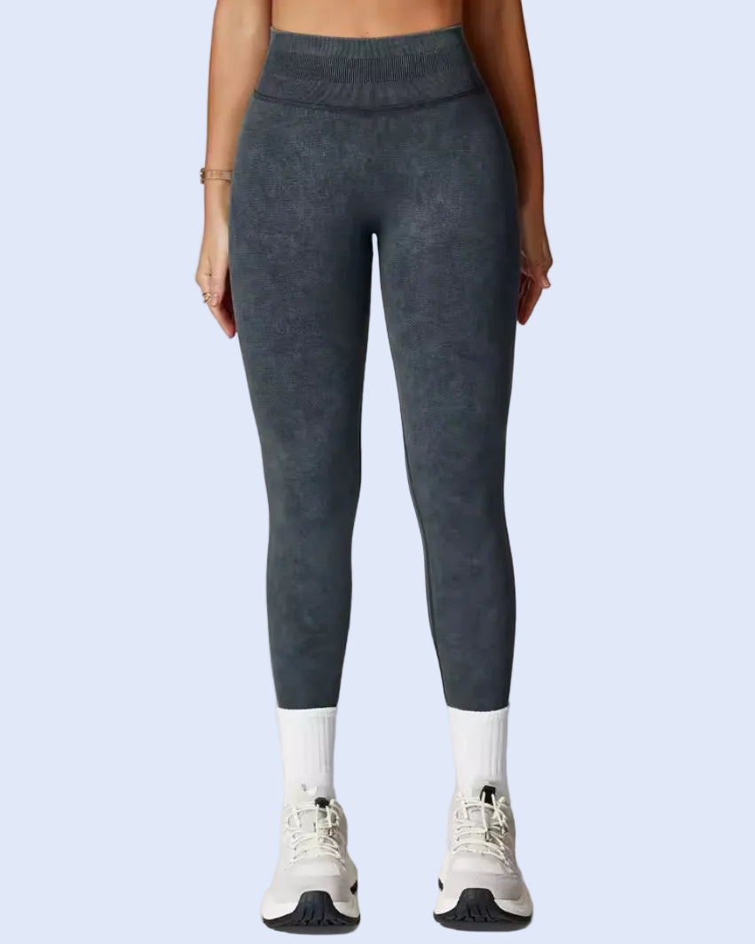 A model from the waist down wearing dark gray textured leggings, white socks, and white sneakers, standing against a light gray studio background.