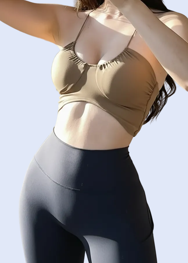 Person wearing a gold sports bra and dark leggings taking a mirror selfie.