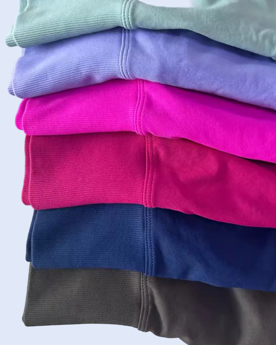 A stack of folded ribbed sweatshirts in multiple colors, including mint green, lavender, hot pink, royal pink, navy blue, and dark gray, shown on a white background.