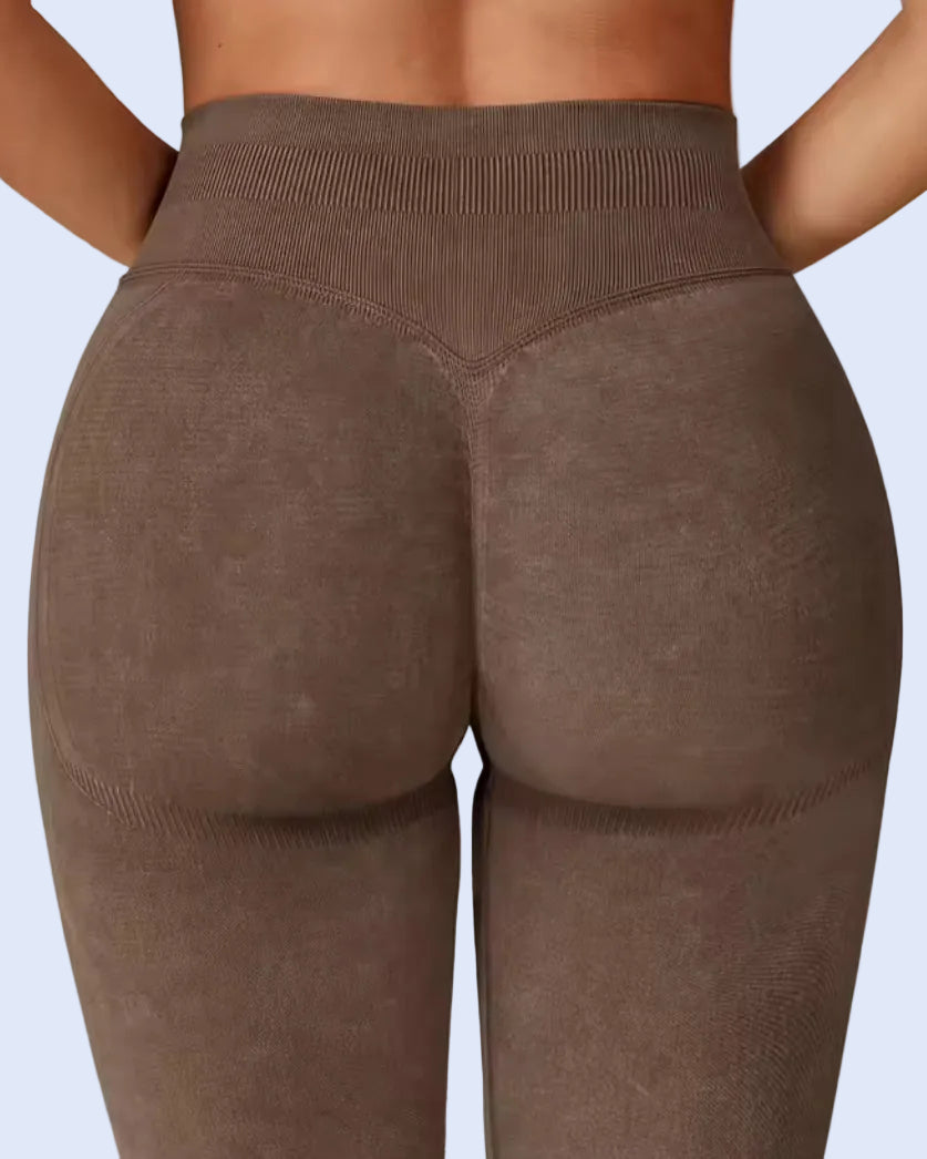 Rear view of a model wearing high-waisted, textured brown leggings against a light gray studio background.