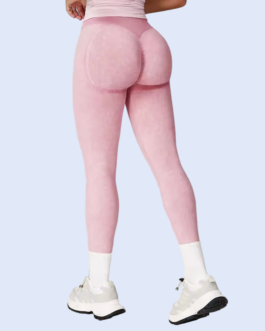Rear view of a model wearing pink high-waisted seamless leggings with a textured pattern, paired with white socks and white sneakers, against a light gray studio background.
