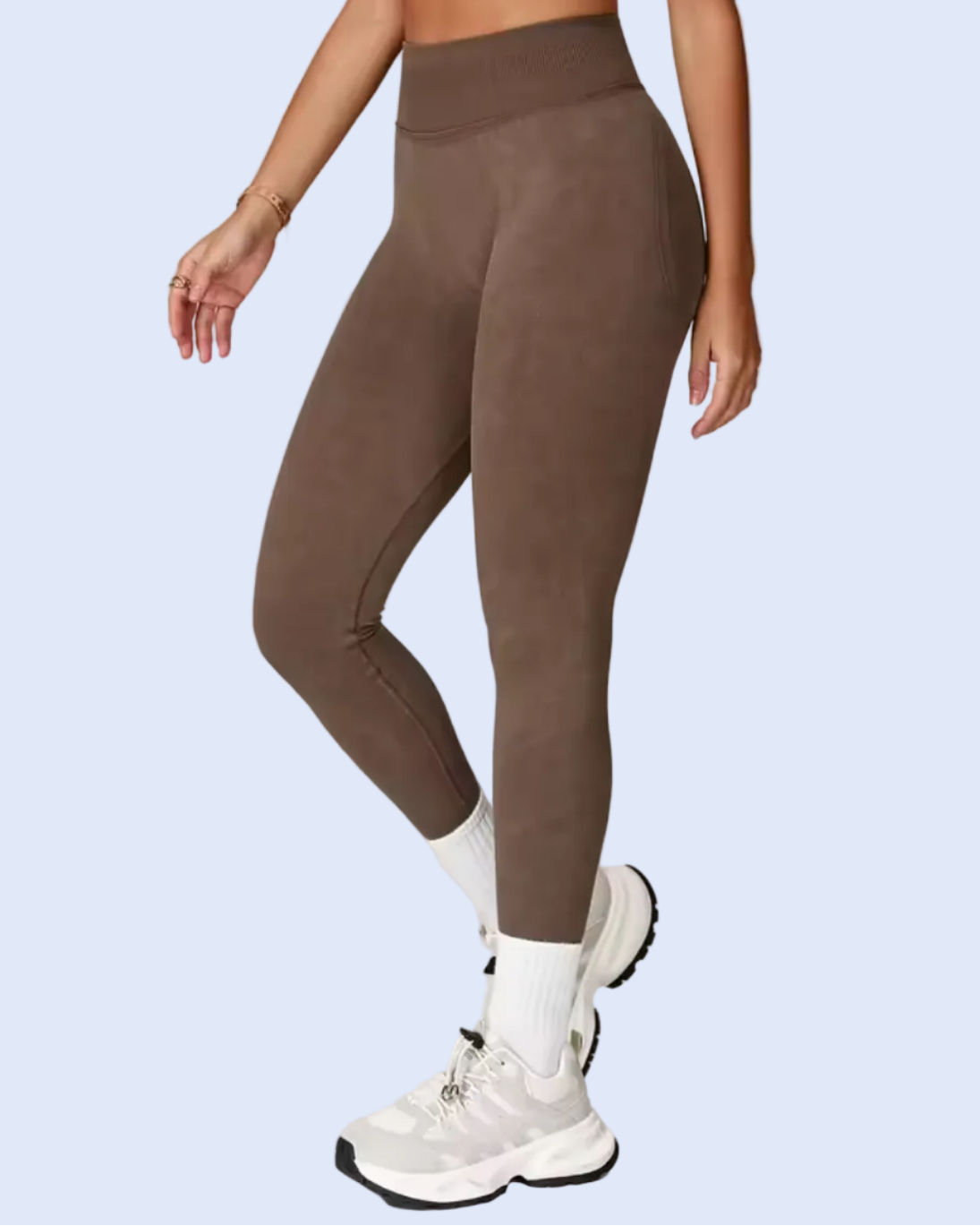 A model wearing high-waisted, ankle-length brown leggings with white socks and white sneakers, shown on a light gray studio background within an e-commerce mobile interface.