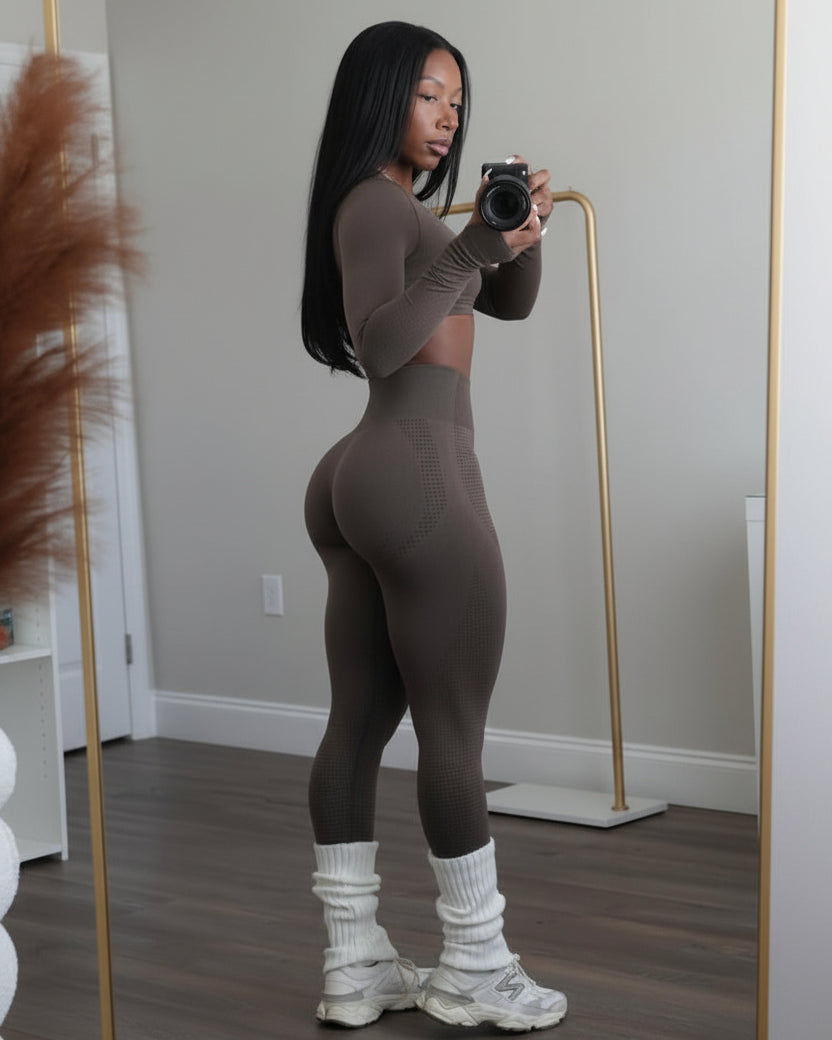 Person taking a mirror selfie wearing a brown outfit in a room with minimal decor.