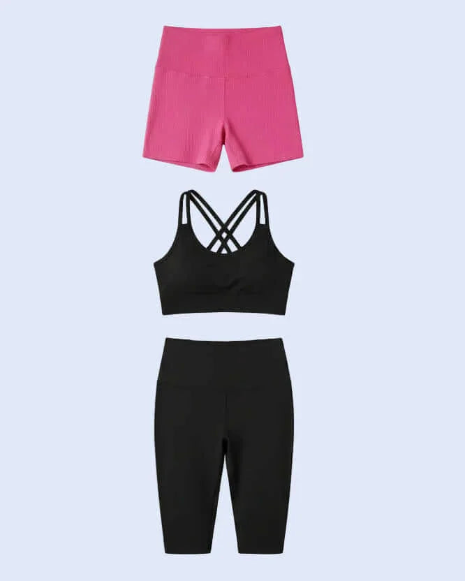 Person taking a mirror selfie in a gym wearing a black sports bra and pink shorts.