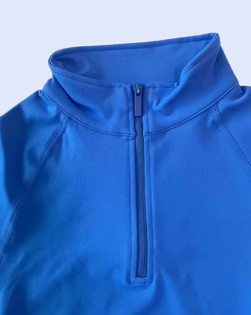 Close-up of a bright blue quarter-zip pullover jacket with a stand-up collar and ribbed zipper, laid flat on a light background.