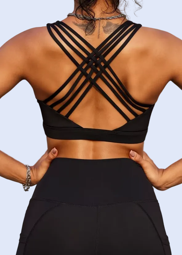 Person wearing a black sports bra and leggings with criss-cross straps on a blurred outdoor background