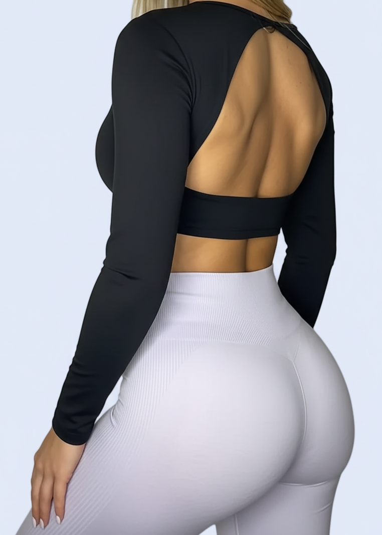 Person wearing a black long-sleeve top with cut-out design and white pants on a plain background