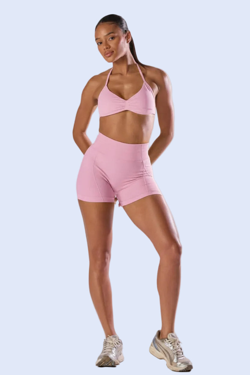 Woman wearing a pink sports bra and shorts set on a white background