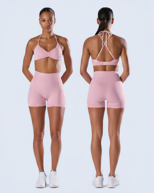 Woman wearing a pink sports bra and shorts set on a white background
