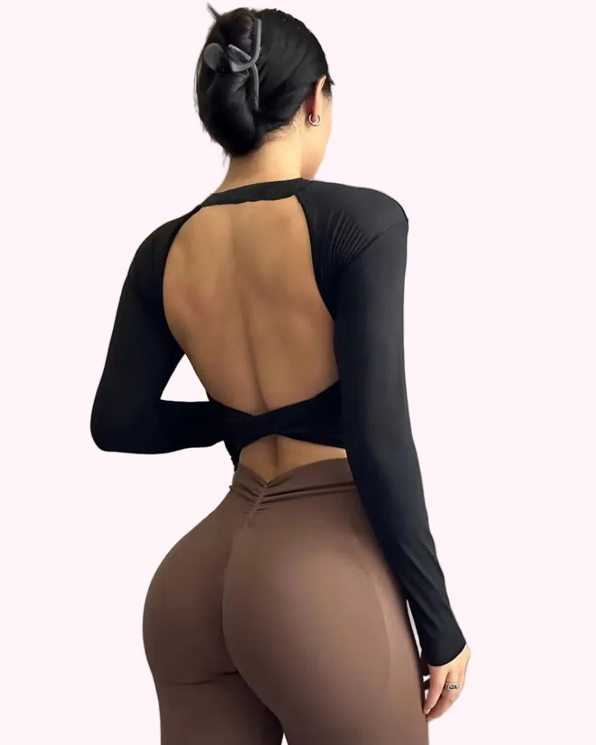 Person wearing a black long-sleeve top and brown leggings against a neutral wall.