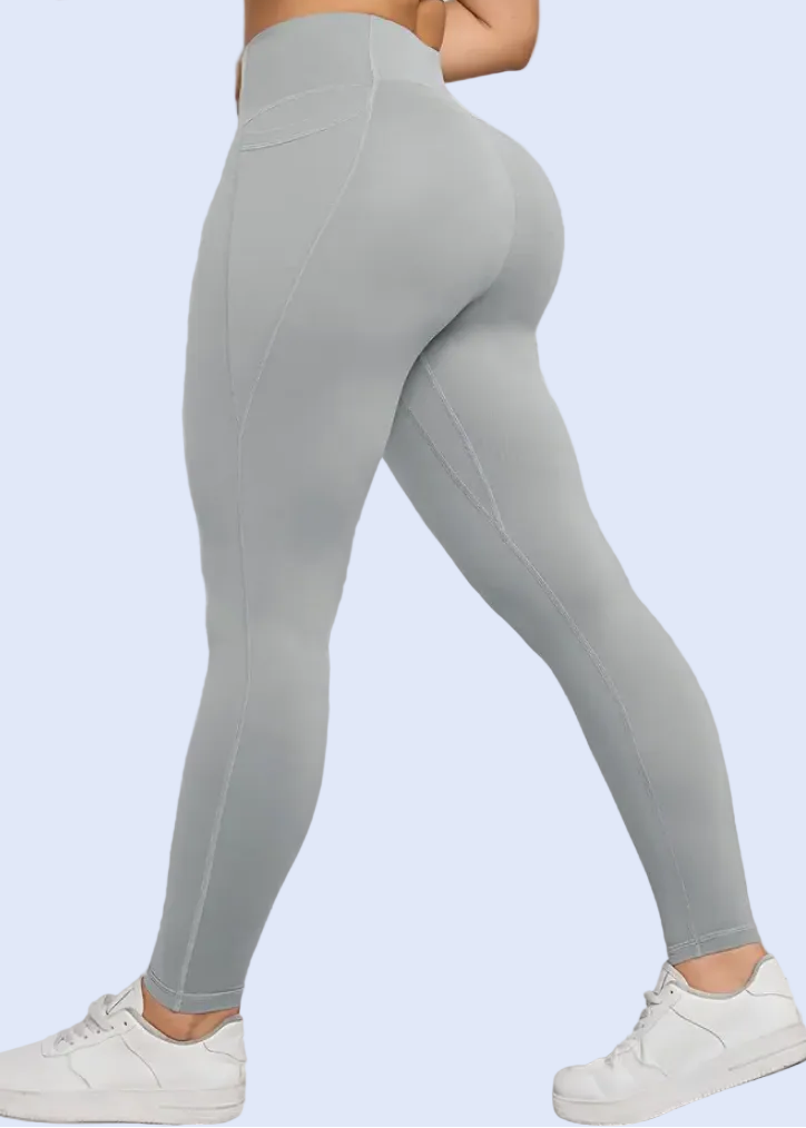 Person wearing gray leggings and white sneakers against a white wall.