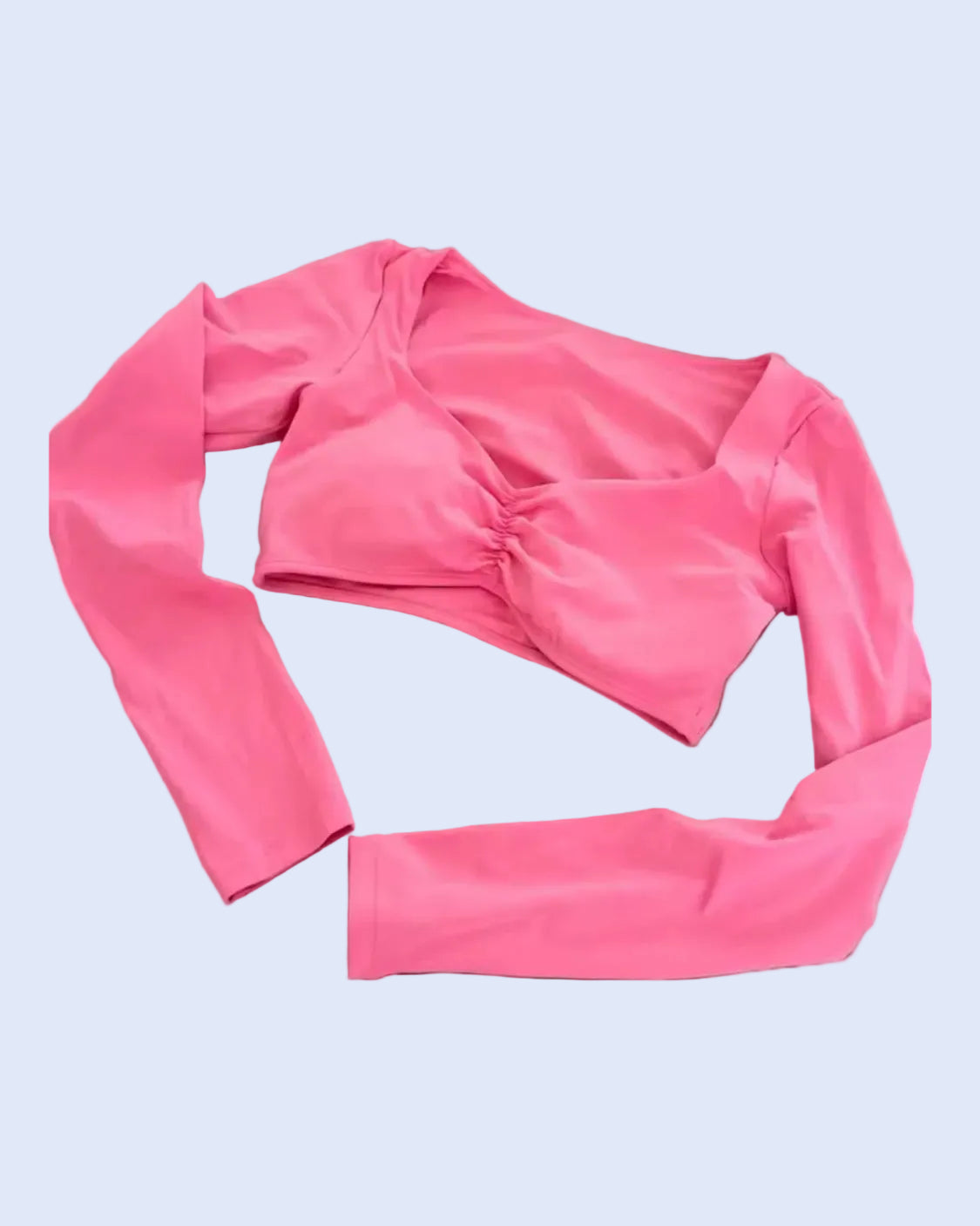 A bright pink long-sleeve crop top with a twisted front detail, laid flat on a gray fabric background.