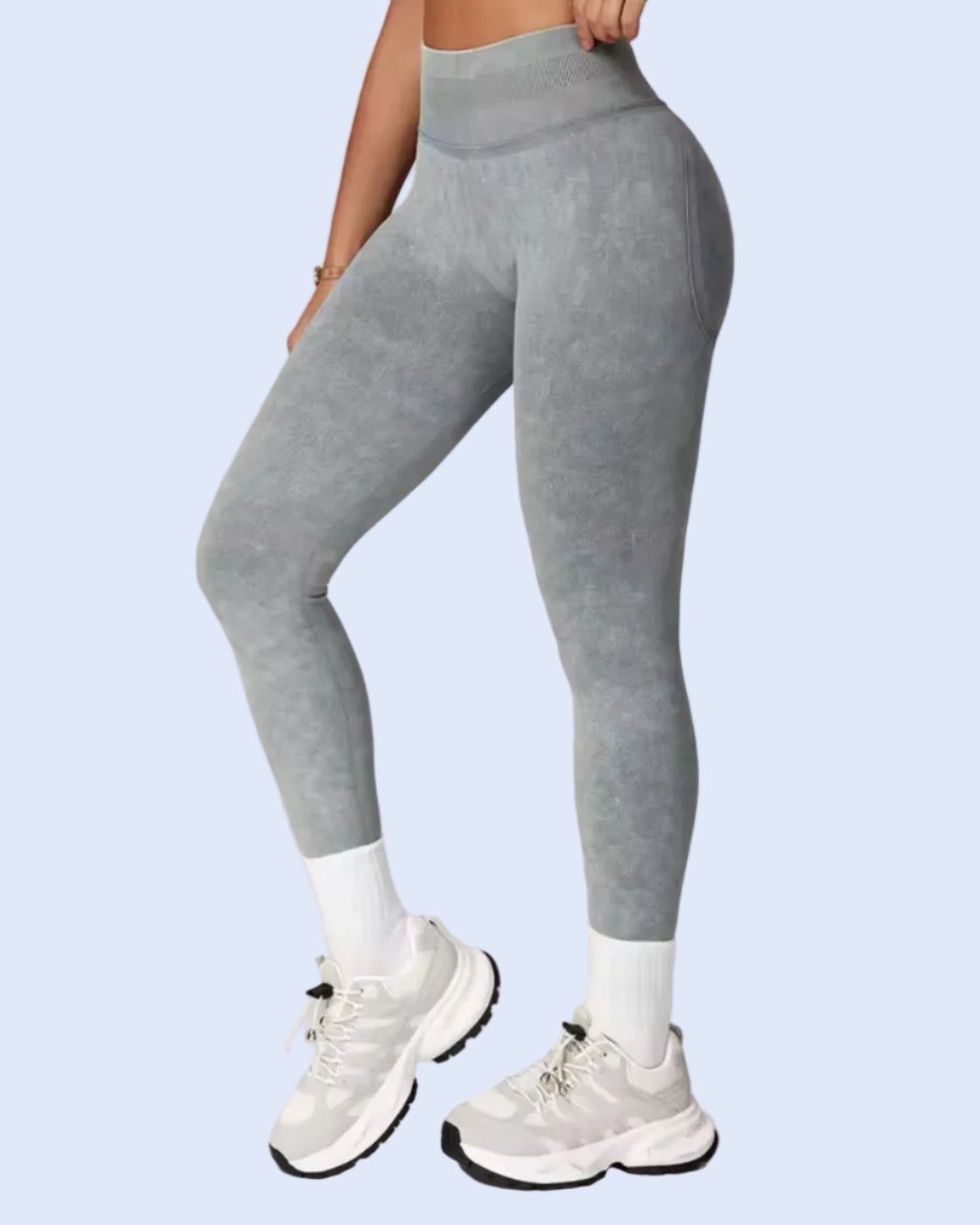 A person modeling high-waisted gray leggings with white socks and white sneakers against a light gray studio background.
