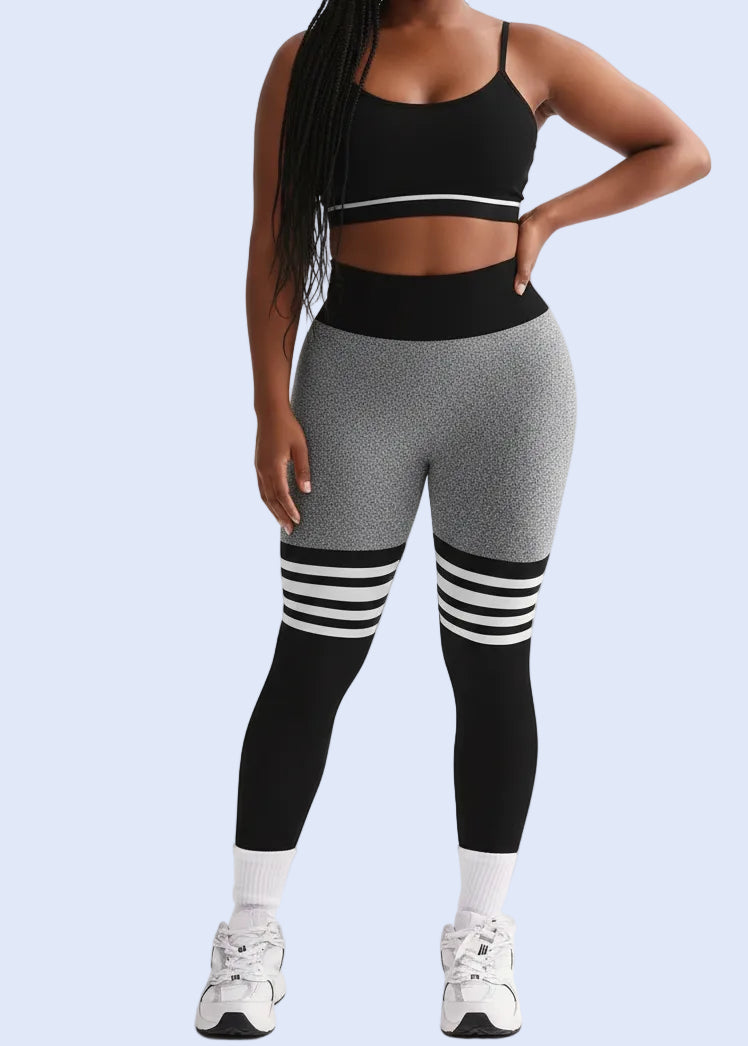 Woman wearing a black sports bra and gray leggings with white accents on a white background