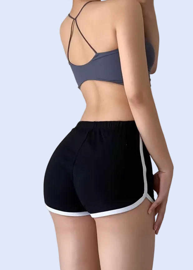 Person wearing a sports bra and shorts taking a mirror selfie on a plain background