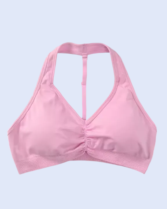 A light pink sports bra with a racerback-style open back and gathered ruching at the center front, shown against a plain light gray background.