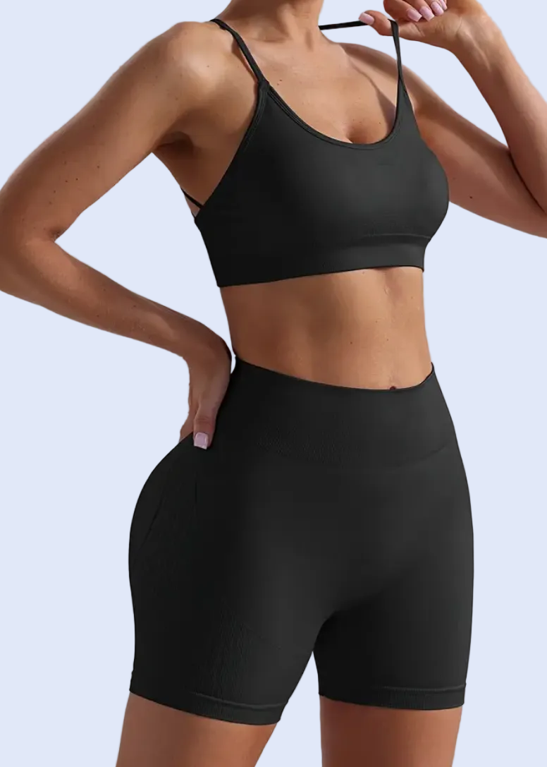 Person wearing a black sports bra and high-waisted shorts on a plain background