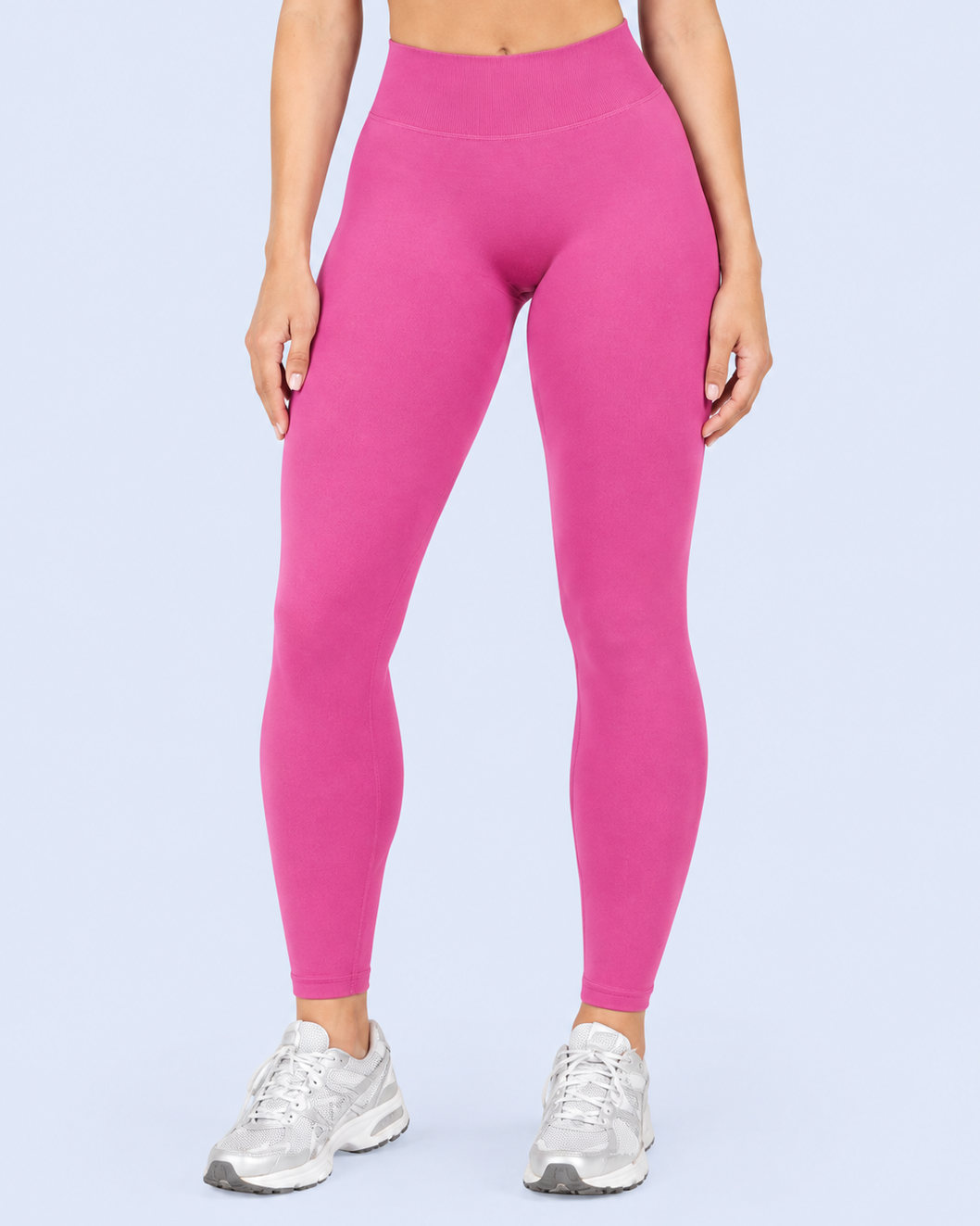 A model wearing bright pink high-waisted leggings and silver athletic sneakers, shown from the waist down against a light blue studio background.