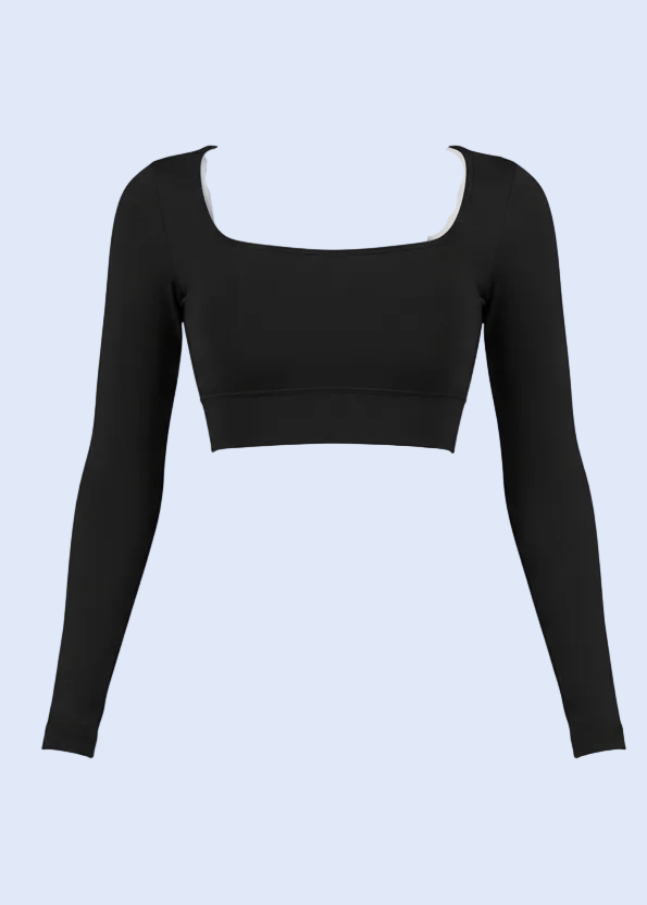 Woman taking a mirror selfie in a gym wearing a black long-sleeve top and light purple shorts.