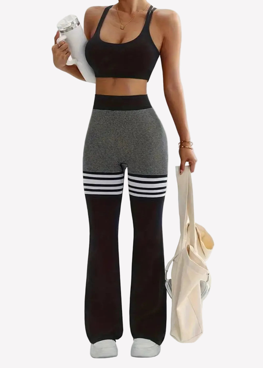 Woman in black sports bra and gray leggings holding a white towel and beige bag on a light background