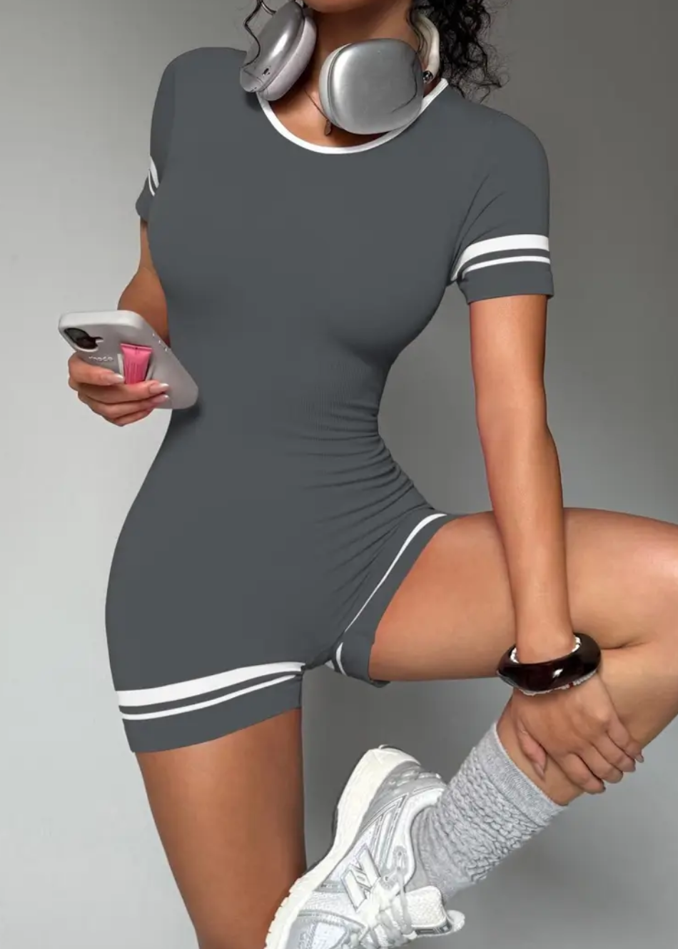 Woman in a gray dress with white accents, holding a phone, on a gray background.