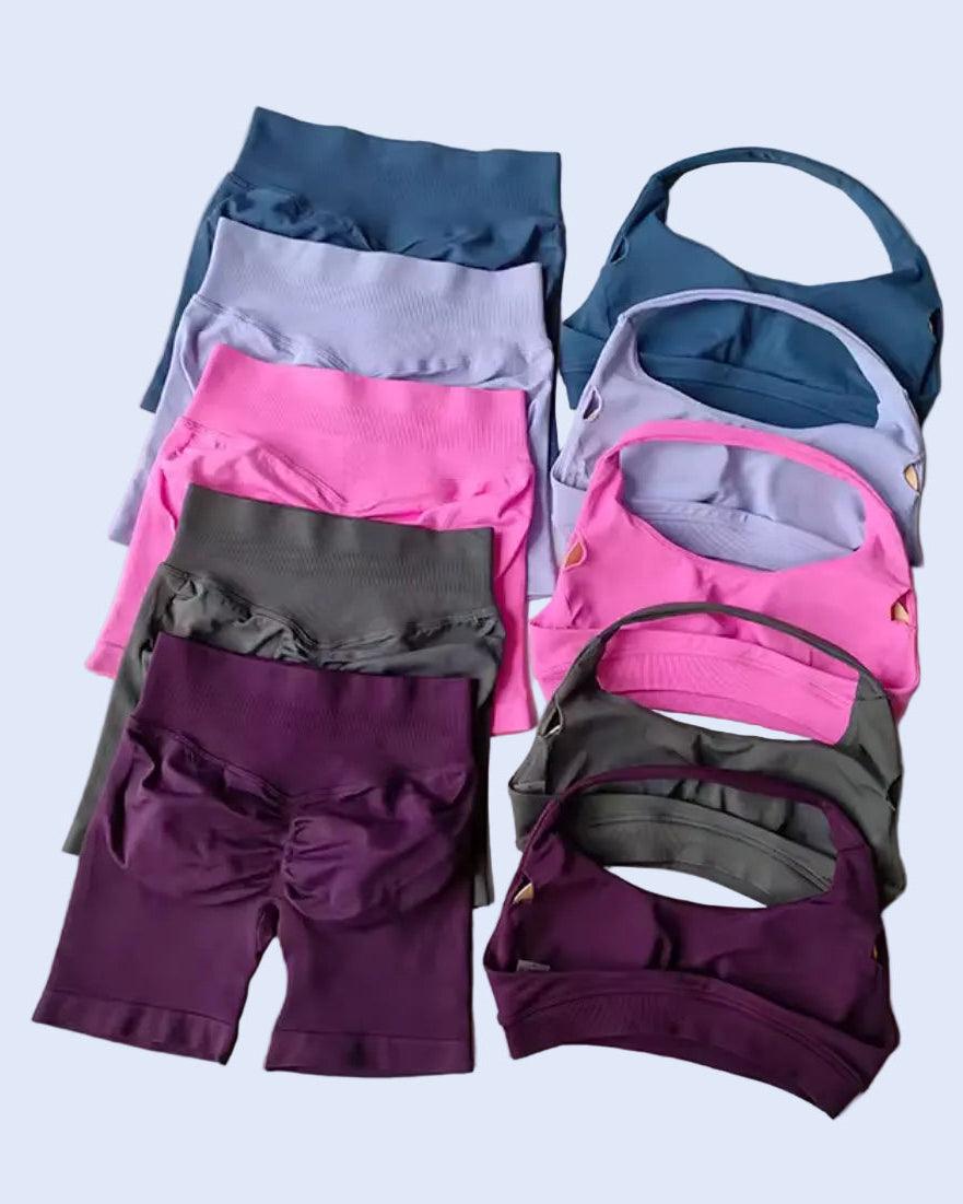 Stack of colorful athletic wear including leggings, sports bras, and shorts on a gray background