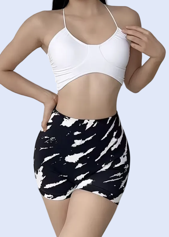 Person wearing a white tank top and black and white patterned shorts on a plain background