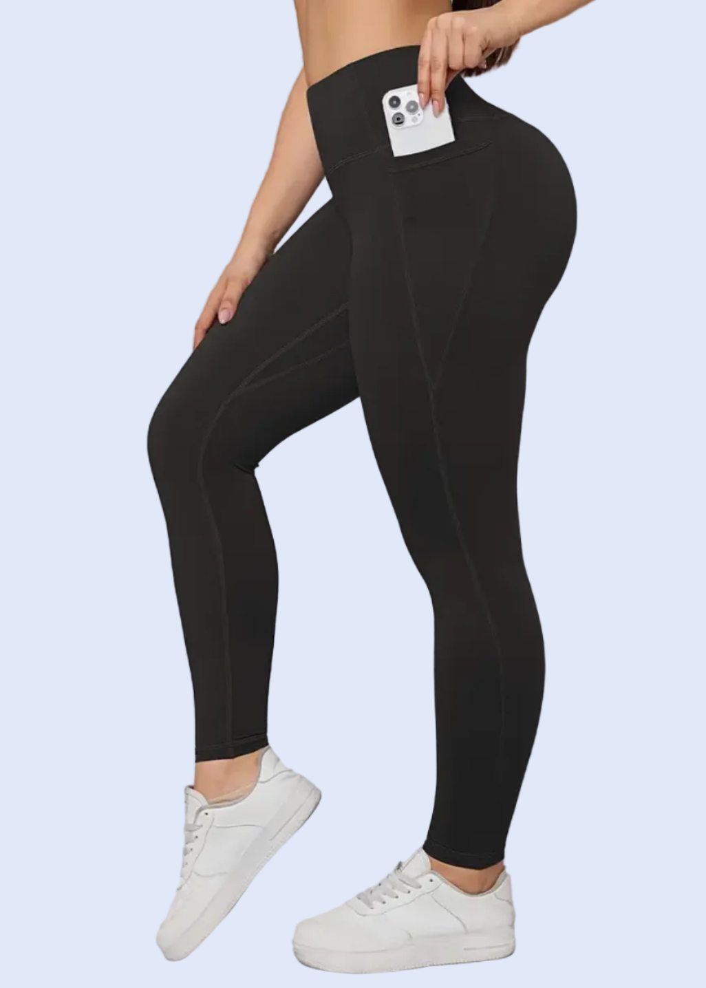 Person wearing black leggings with a white background, showing product details on a smartphone screen.