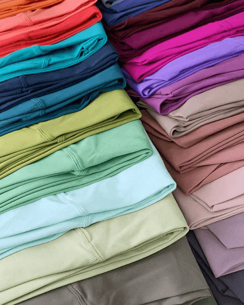 Stacks of folded leggings in a variety of colors, including coral, teal, navy, olive green, mint, light blue, pink, mauve, and gray, arranged diagonally.