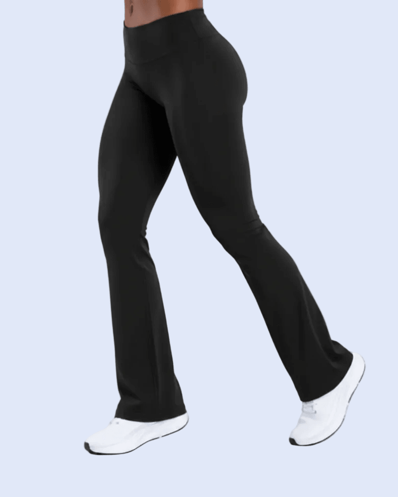Black high-waisted flared leggings shown on a model from the waist down, paired with white sneakers, against a light blue background.