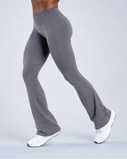 A person modeling high-waisted gray flared leggings with white sneakers against a light gray studio background.