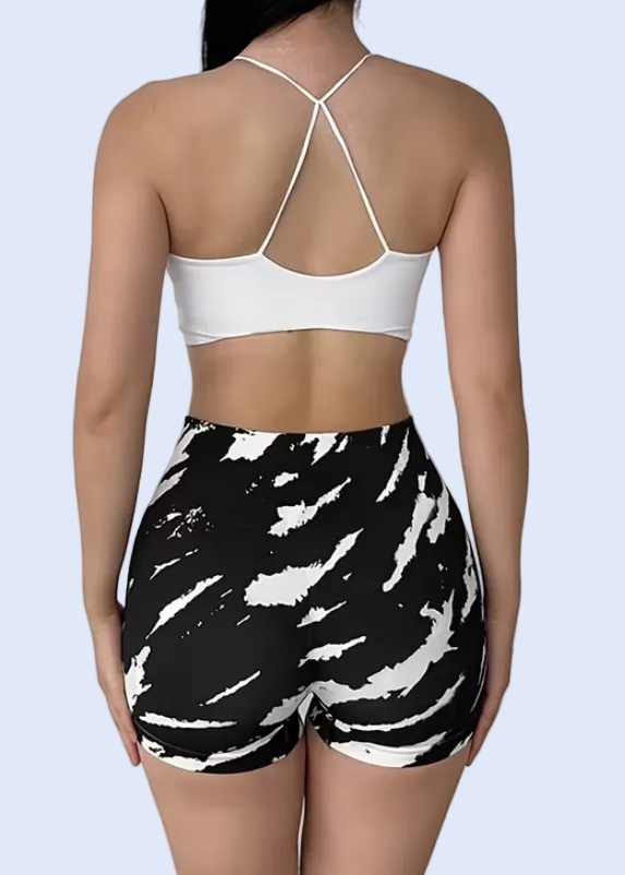Person wearing a white sports bra and black and white patterned shorts on a plain background