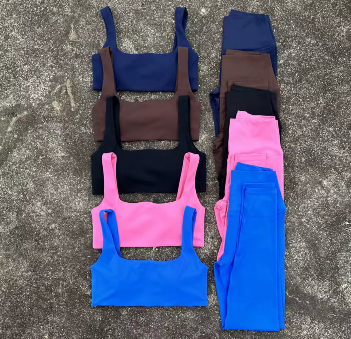 Six pairs of activewear laid flat on a gray concrete surface, arranged in two columns. The left column shows sports bra tops in navy, brown, black, and bright pink.
