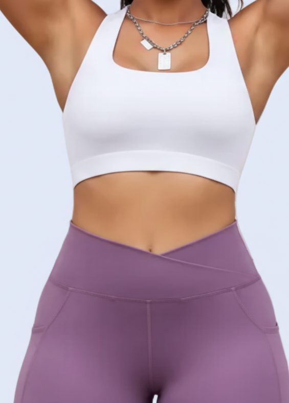 Woman in white sports bra and purple leggings posing outdoors.
