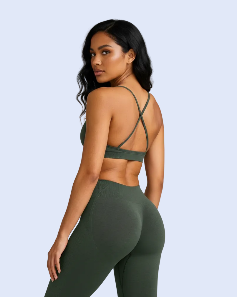 A woman modeling an olive green athletic set, featuring a sports bra with crisscross back straps and high-waisted leggings, shown from a three-quarters back view against a solid gray background.