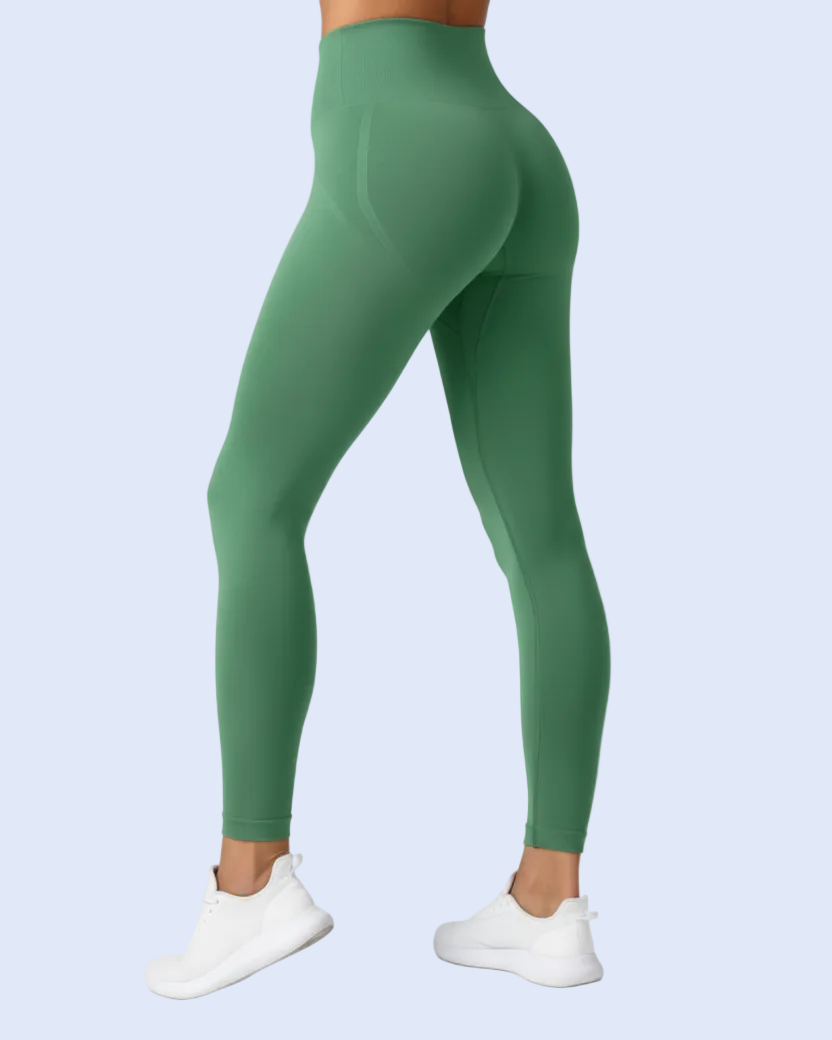 A model from the back wearing high-waisted green leggings and white sneakers, shown against a light blue studio background.