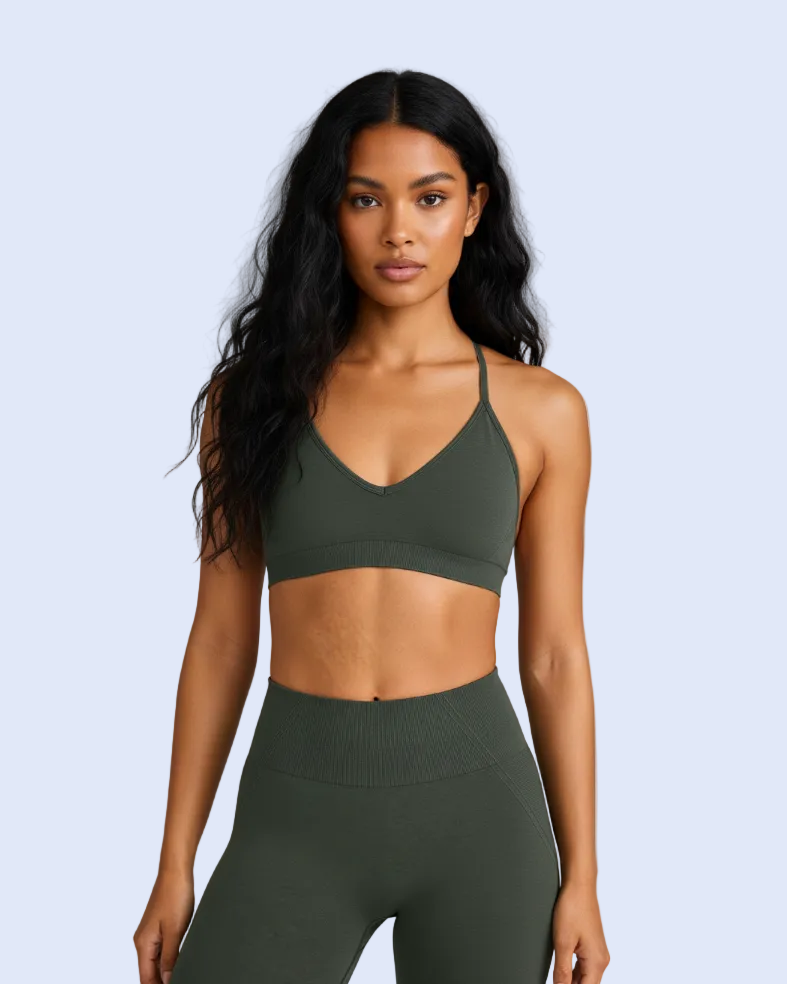 A woman modeling an olive green sports bra and matching high-waisted leggings against a light gray studio background.